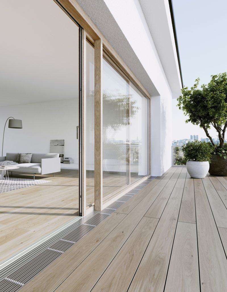 Minimalist architectural home with timber lift and slide doors opening onto a city-facing terrace, showcasing flush threshold detailing and wide-plank timber flooring — part of a bespoke exterior glazing and interiors living space.
